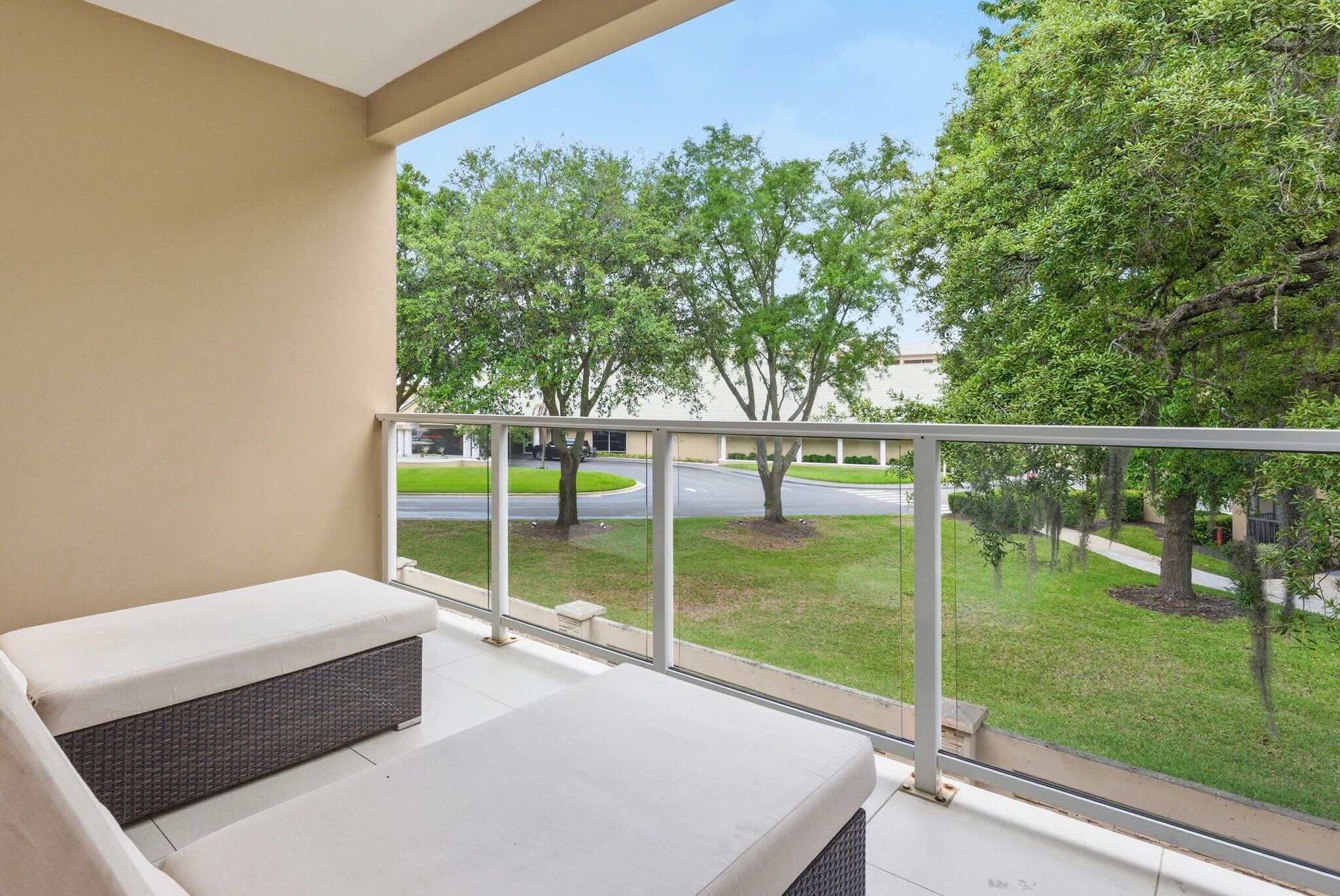 A balcony with a white cushioned bench, a metal railing, and a view of a green landscape with trees and a road.