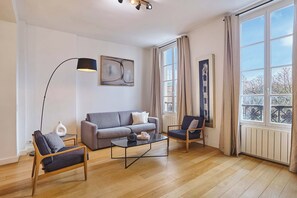 Ein modernes Wohnzimmer mit einer Couch, zwei Sesseln, einem Couchtisch, einer Stehlampe und Kunstwerken an den Wänden.