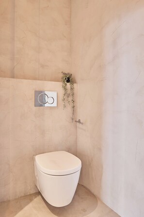 Ein Badezimmer mit Toilette, Wandarmatur und einer kleinen Pflanze.