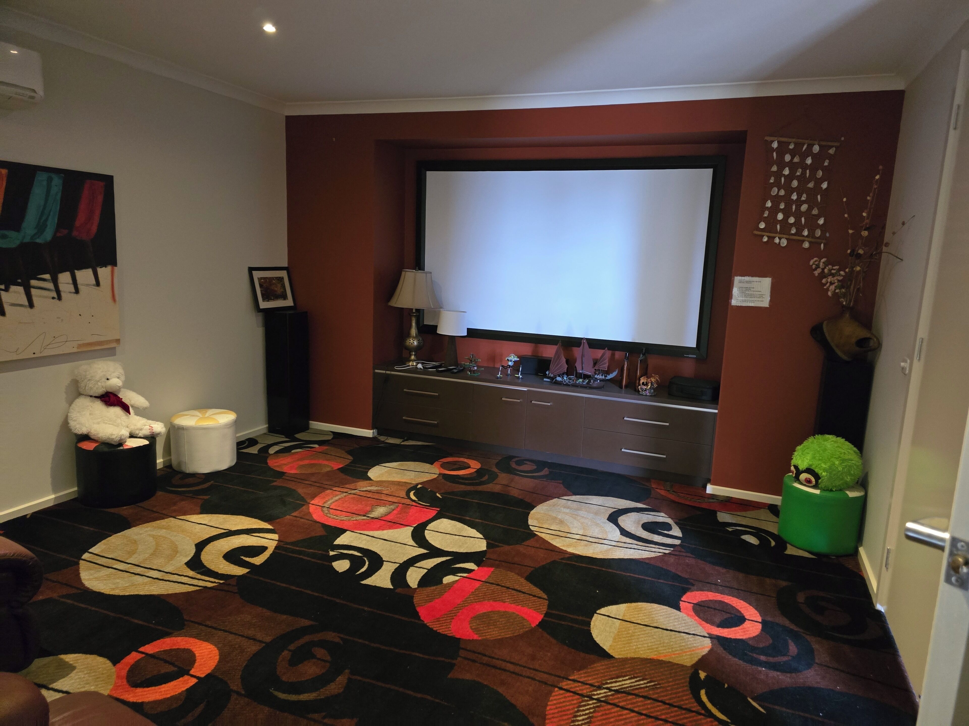 Habitación de hotel con una televisión de pantalla plana grande, un escritorio con lámpara, un peluche y una alfombra estampada.