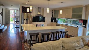 Een moderne keuken met een centraal eiland, barkrukken, een koelkast en een zithoek met een bank.