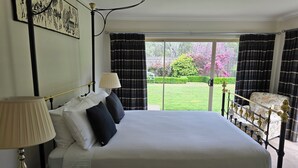 Een slaapkamer met een bed, twee bedlampen, een raam met gordijnen en uitzicht op een tuin.