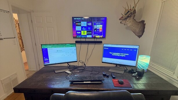 Un espace de travail aménagé à la maison, comprenant un bureau, trois écrans, un clavier, une souris et une chaise.
