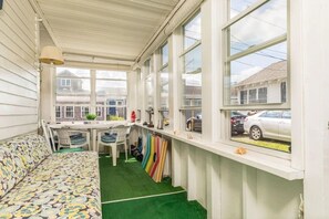 A sunroom with a sofa, a dining table, chairs, a small kitchen area, and large windows. - Hybiscus - 2 BR - 2 Pets - BBQ -Parking - Walk to Beach & Hampton Strip (Hampton)