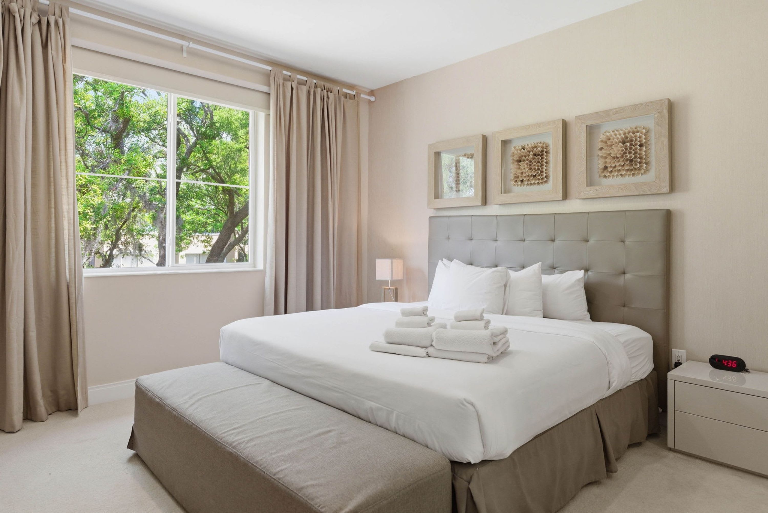 Une chambre d’hôtel avec un grand lit, une table de chevet, une commode et une fenêtre avec des rideaux.