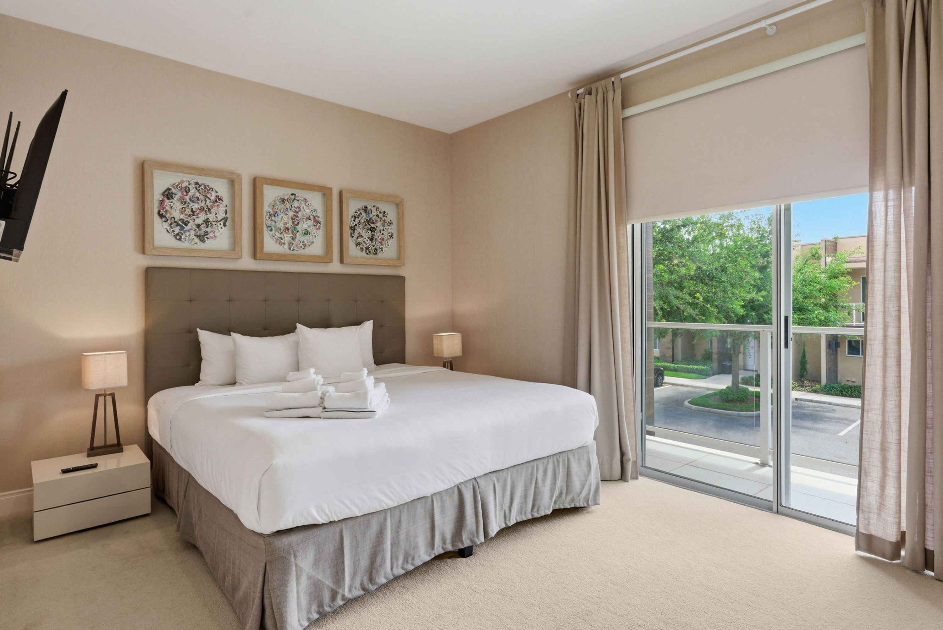 A hotel room with a large bed, a nightstand, a lamp, and a view of the outside.