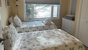 A bedroom with two beds, a window with a view, a ceiling fan, and a dresser.