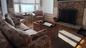 A living room with a sofa, armchairs, a fireplace, a television, and large windows.