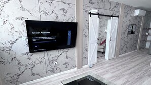 A modern bathroom with a marble wall, a glass shower enclosure, and a mounted television displaying 'Remote & Accessories' instructions. - Beautiful Hideaway with pool close to hiking, waterfalls and Culebra ferry (Ceiba)