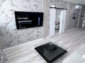 Ein modernes Badezimmer mit Marmorwand, einer Duschkabine aus Glas und einem an der Wand montierten Fernseher, der eine Anleitung für 'Remote & Accessories' anzeigt.