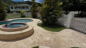 Piscina com hidromassagem, cercada por uma área arenosa e palmeiras.