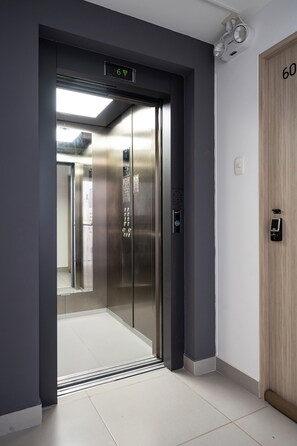 Un ascenseur doté d’un écran numérique, une porte en bois avec une serrure et un sol carrelé.