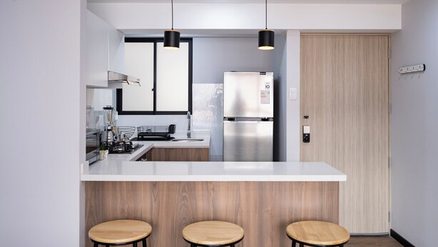 A modern kitchen with a white countertop, stainless steel appliances, wooden stools, and pendant lighting. - Serene 2-bedroom apartment in charming Cusco near historic sites (Cusco)