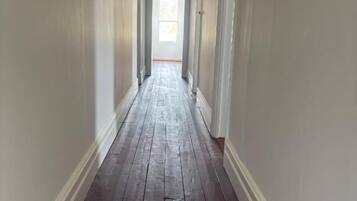 A long, narrow hallway with a wooden floor and white walls, leading to a door at the end.