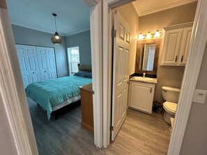 Ein Schlafzimmer mit Bett, Nachttisch, Kommode, Spiegel und einem Badezimmer mit Waschbecken und Toilette.