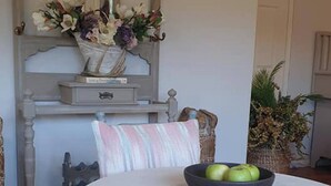 Un comedor con una mesa redonda, sillas, un cuenco de manzanas verdes y un espejo decorativo colgando arriba.