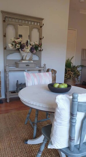 A dining area with a round table, chairs, a bowl of green apples, and a decorative mirror above. - Room-stylish Studio in Reedy Creek (Gold Coast)