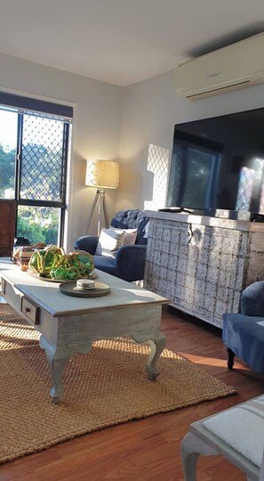 A living room with a sofa, a coffee table, a lamp, and a television. - Room-stylish Studio in Reedy Creek (Gold Coast)