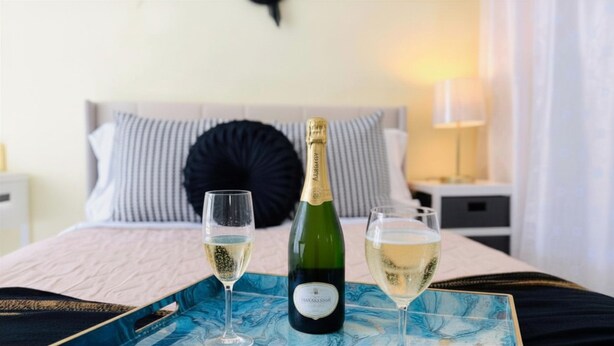 Ein Bett mit einem gestreiften Kopfkissen, einer Champagnerflasche und zwei Gläsern auf einem Tablett.