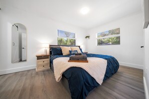 A bedroom with a bed, bedside tables, a mirror, and windows with blinds. - Modernized 3BR Pool Home near downtown, i75, & WEC (Ocala)