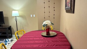 Un comedor con una mesa redonda, sillas amarillas, mantel rojo, un centro de mesa decorativo, una lámpara de pared y un cuadro enmarcado.