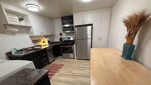 Una cocina moderna con armarios blancos, electrodomésticos de acero inoxidable, una mesa de comedor de madera y una planta decorativa.