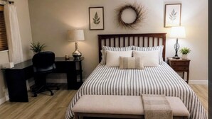 Un dormitorio con cama, mesitas de noche, escritorio, silla, banco y adornos en la pared.