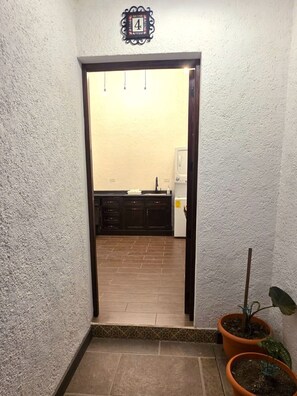 A narrow hallway leading to a kitchen with dark cabinets, a white refrigerator, and a potted plant. - Peaceful 1-bedroom apartment in the heart of Antigua Guatemala (Antigua Guatemala)