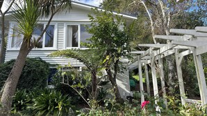 Una casa blanca con porche, rodeada de plantas y árboles.