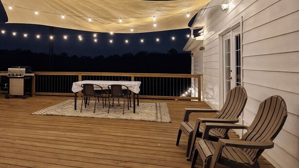 An outdoor deck with a table and chairs, string lights, and a grill. - Farmhouse in Dawsonville-Perfect for groups! (Dawsonville)