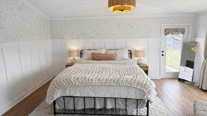 A bedroom with a bed, two bedside tables, a hanging light fixture, and a door leading outside. - Farmhouse in Dawsonville-Perfect for groups! (Dawsonville)