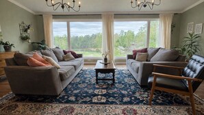 A living room with two sofas, a coffee table, and a chair, with a large window and curtains. - Farmhouse in Dawsonville-Perfect for groups! (Dawsonville)