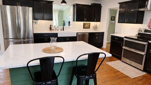 A kitchen with dark cabinets, a stainless steel refrigerator, a double oven, and a large island with two chairs. - Farmhouse in Dawsonville-Perfect for groups! (Dawsonville)