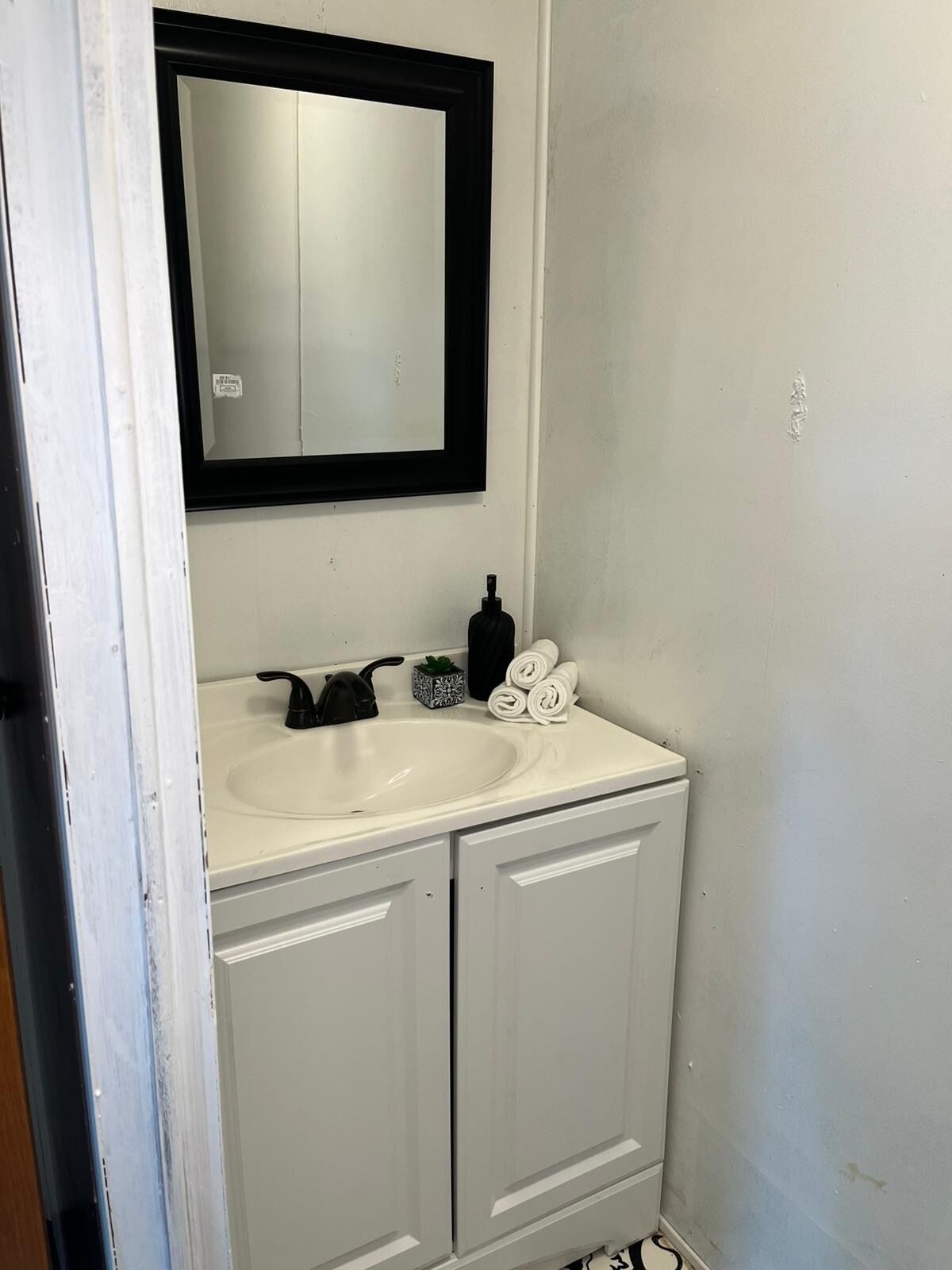 Une salle de bain avec un lavabo blanc, un robinet noir et un miroir au-dessus. On y trouve des serviettes et un distributeur de savon sur le comptoir du lavabo.