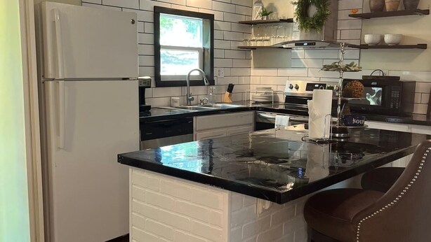A kitchen with a white refrigerator, a black countertop island, and a microwave. - Arbuckle Lake Hideaway (Sulphur)