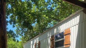 A single-story building with a corrugated metal exterior, two windows with wooden shutters, and a paved pathway leading to the entrance. - Arbuckle Lake Hideaway (Sulphur)