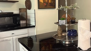 A kitchen with a black countertop, a microwave, a stove, a shelf with pottery, a painting, and a decorative stand with a plant. - Arbuckle Lake Hideaway (Sulphur)