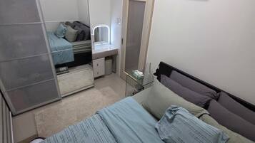 A bedroom with a bed, a vanity with a mirror, a wardrobe, and a small table with a lamp.