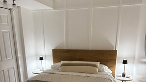Een net opgemaakt bed met een gewatteerd sprei, een houten hoofdbord en twee nachtkastjes met lampen.