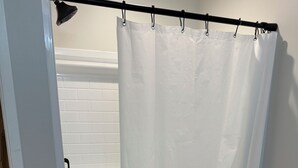 Een douchegordijn in een badkamer met witte betegelde wanden en een zwarte mat op de vloer.