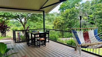 A wooden deck with a table and chairs, a hammock, and a view of lush greenery.