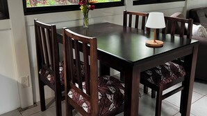 Zona pranzo con tavolo, sedie, un vaso con fiori e ampie finestre vista su vegetazione.