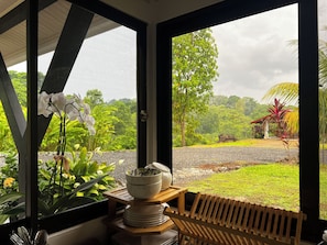 A room with a view of a lush landscape, a wooden bench, and a table with a bowl and plates.