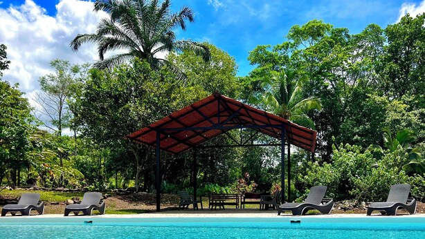 Una piscina trasparente con lettini prendisole e un padiglione ombreggiato.