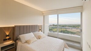 A bedroom with a large bed, a nightstand, a wall-mounted light, and a window with a view. - Luxury Apartment Suite in Santa Marta | Ocean View (Santa Marta)