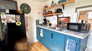 Een keuken met een zwarte koelkast, blauwe keukenkastjes, een magnetron en diverse keukenspullen op planken.