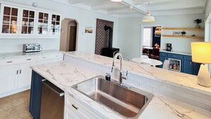 Una cocina amplia con armarios blancos, encimera de mármol, lavavajillas integrado y un revestimiento de pared de ladrillo.