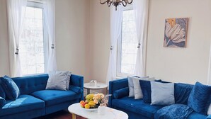 Una sala de estar con dos sofás azules, una mesa de centro blanca, una araña y un aire acondicionado instalado en la pared.