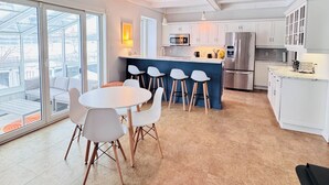 Una cocina moderna con armarios blancos, un refrigerador de acero inoxidable y un comedor con una mesa redonda y sillas.
