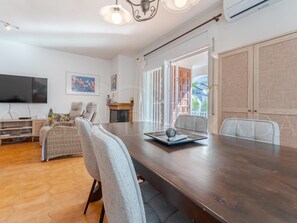 A modern living room with a dark wooden dining table, grey upholstered chairs, a flat-screen TV, and a fireplace.